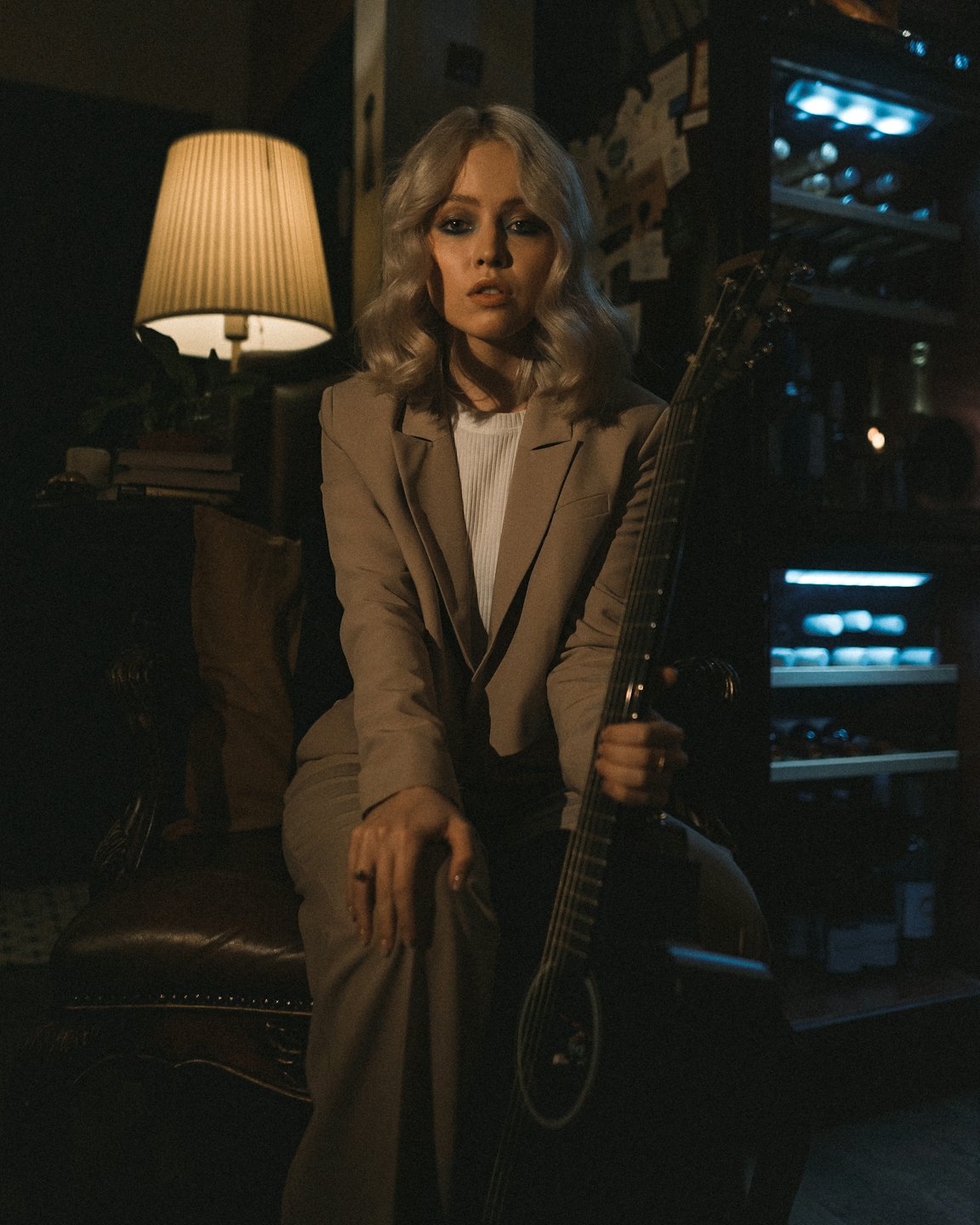 Woman in a beige suit holding an acoustic guitar.