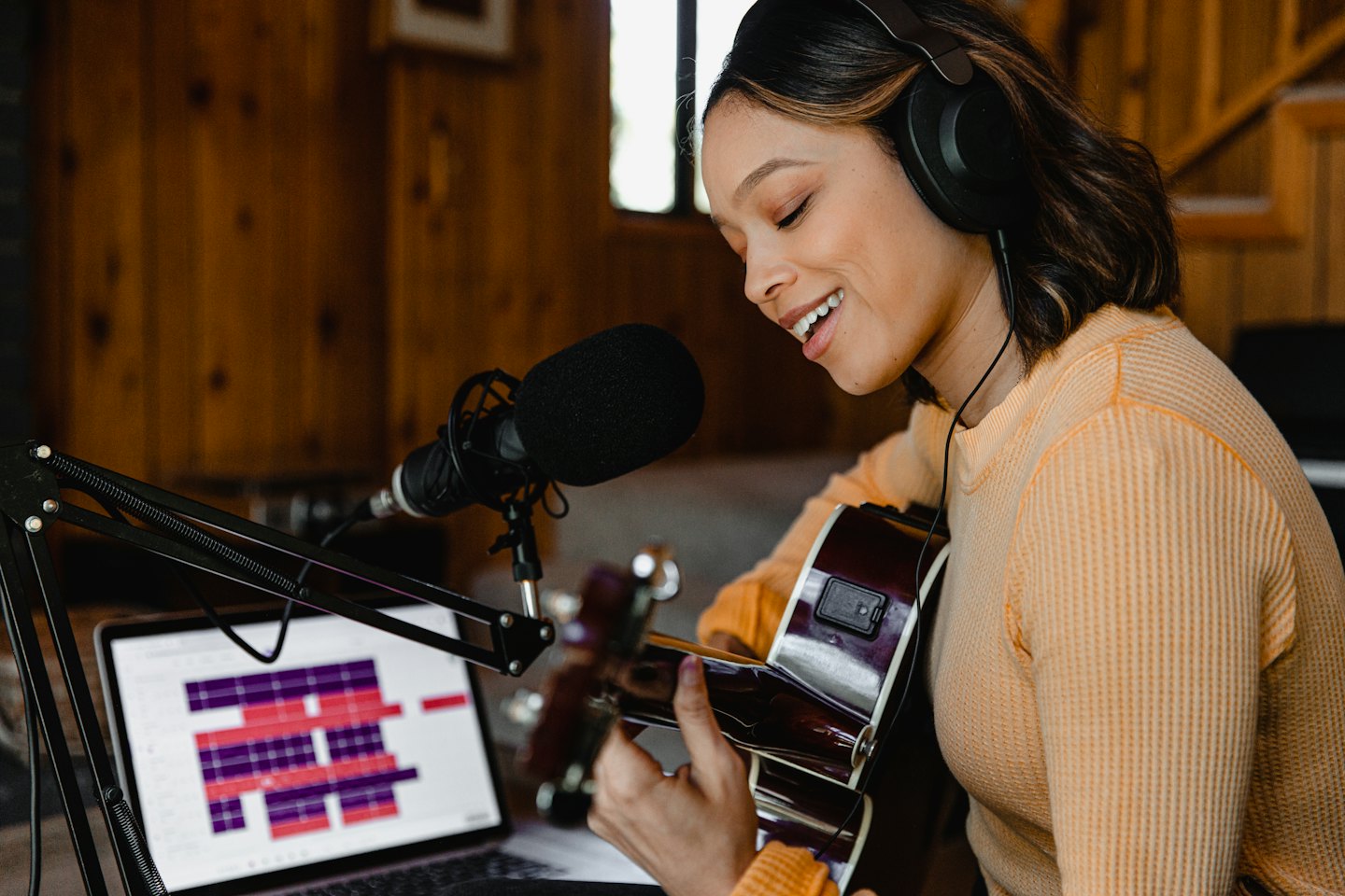 Woman singing into a microphone while recording guitar music.