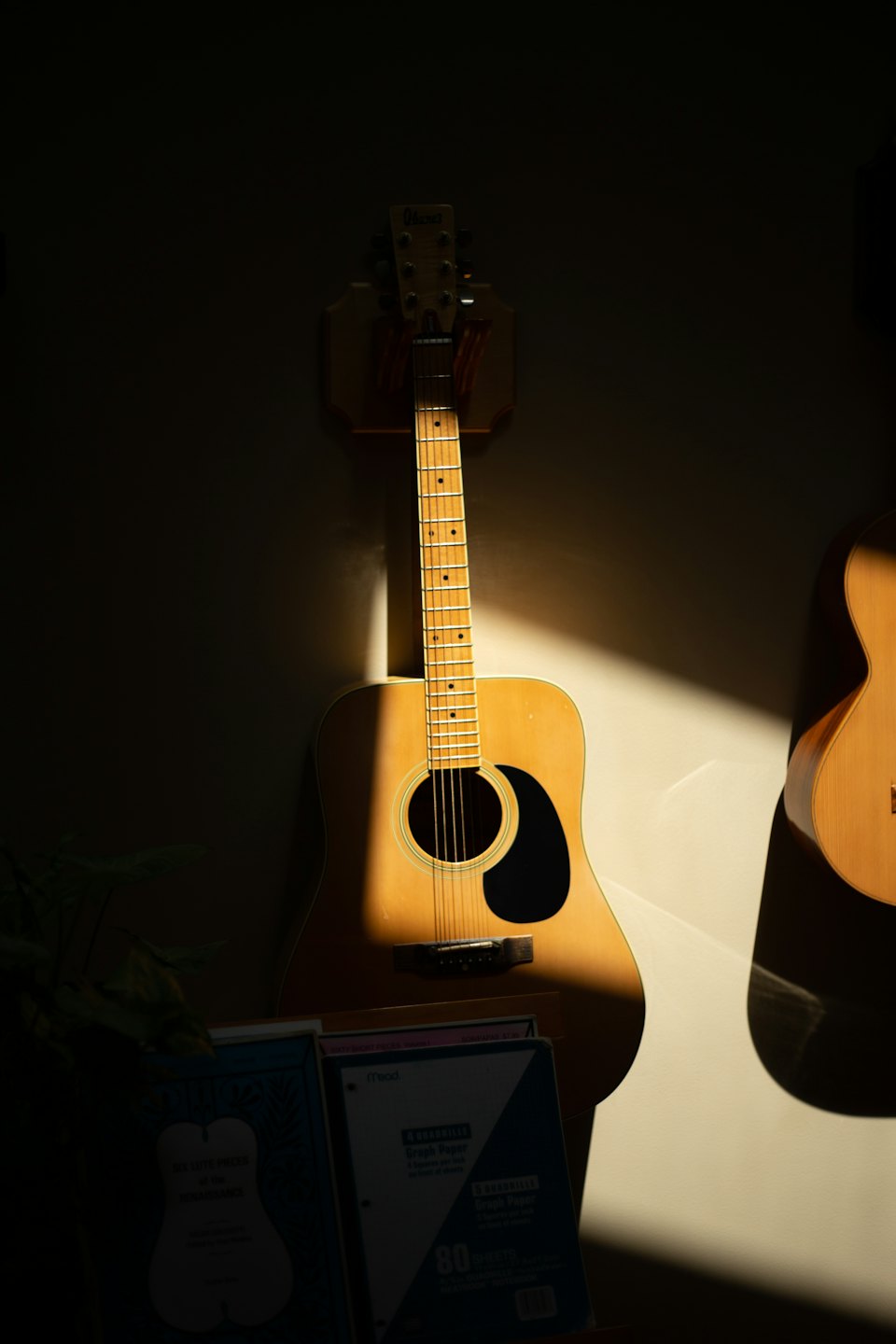 Acoustic guitars hang on a wall above stacked music books.